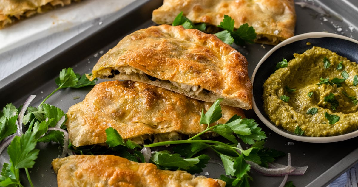 Fette di pesto di pollo calzone su una teglia grigia accanto a una ciotola di pesto