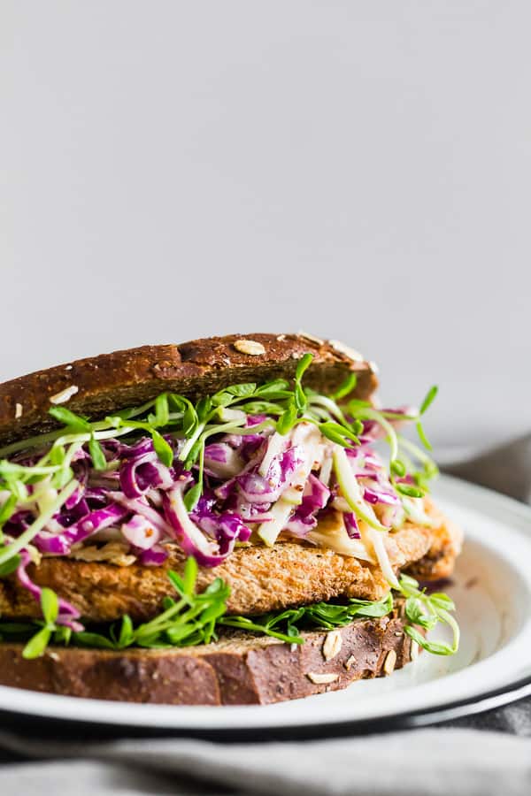 Questo panino croccante di pollo con cavolo di mele e cavolo di mele prende i sapori dell'autunno e li mette in un panino. È una cotoletta di pollo croccante perfettamente cotta condita con formaggio Gouda affumicato, germogli di piselli e insalata di cavolo rosso e mela piccante. Adorerai questo panino assassino.