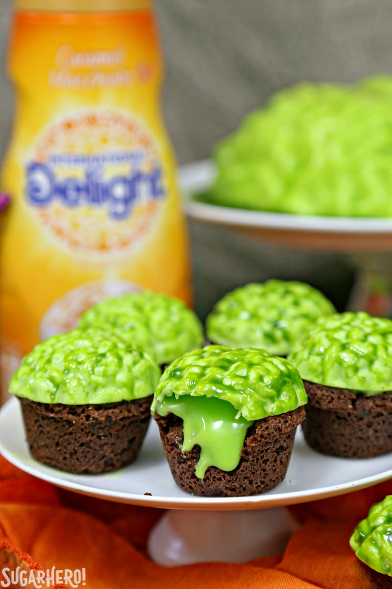 Zombie Brain Brownie Bites - con un grande cervello verde dietro e una bottiglia di crema al caffè al caramello | Da SugarHero.com