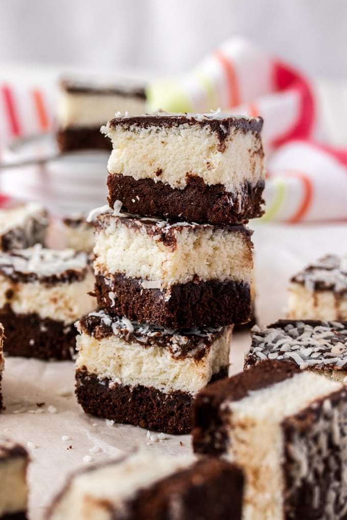 Amantes del coco, ¡esta receta de Easy Chocolate Coconut Brownies es solo para ti! Un brownie de chocolate riquísimo y rico, un relleno de coco pegajoso y una cobertura de ganache pegajoso. Se podría llamar casi llamarlos brownies de recompensa. Una pila de 3 brownies de coco con otros a su alrededor.