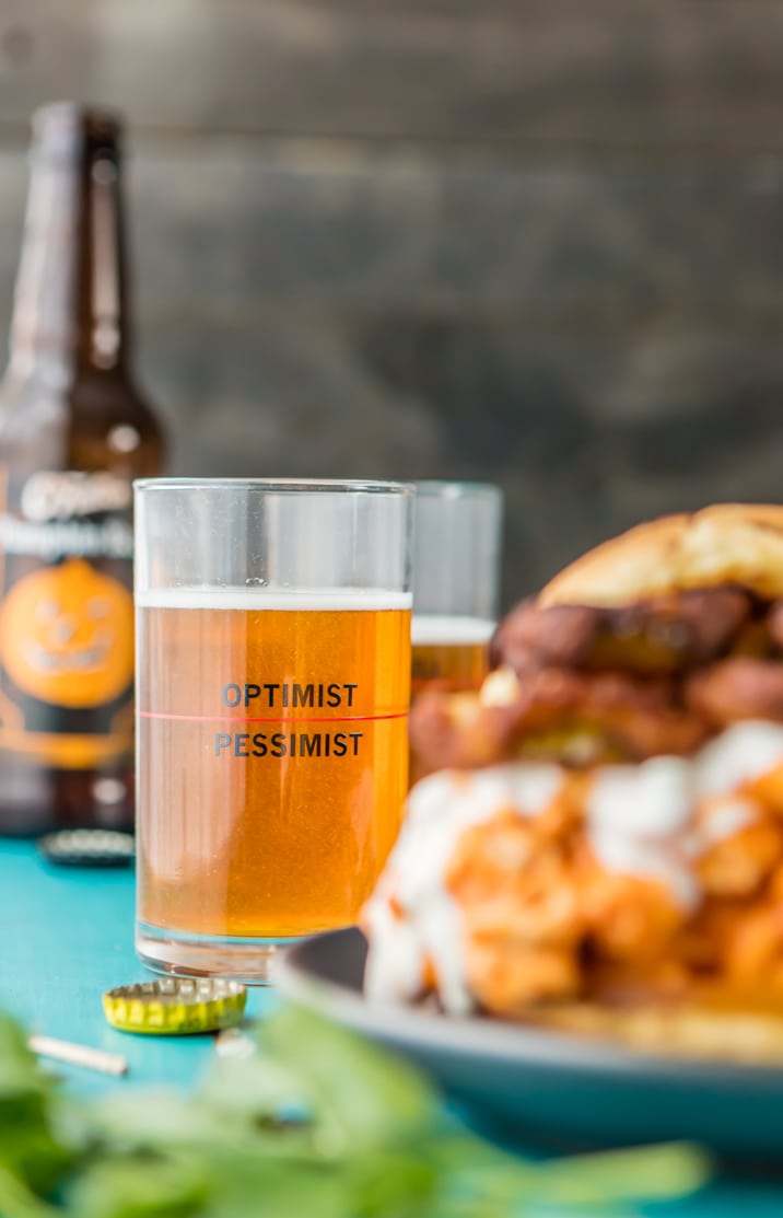 vaso de cerveza en foco, sandwich de pollo búfalo borrosa en primer plano