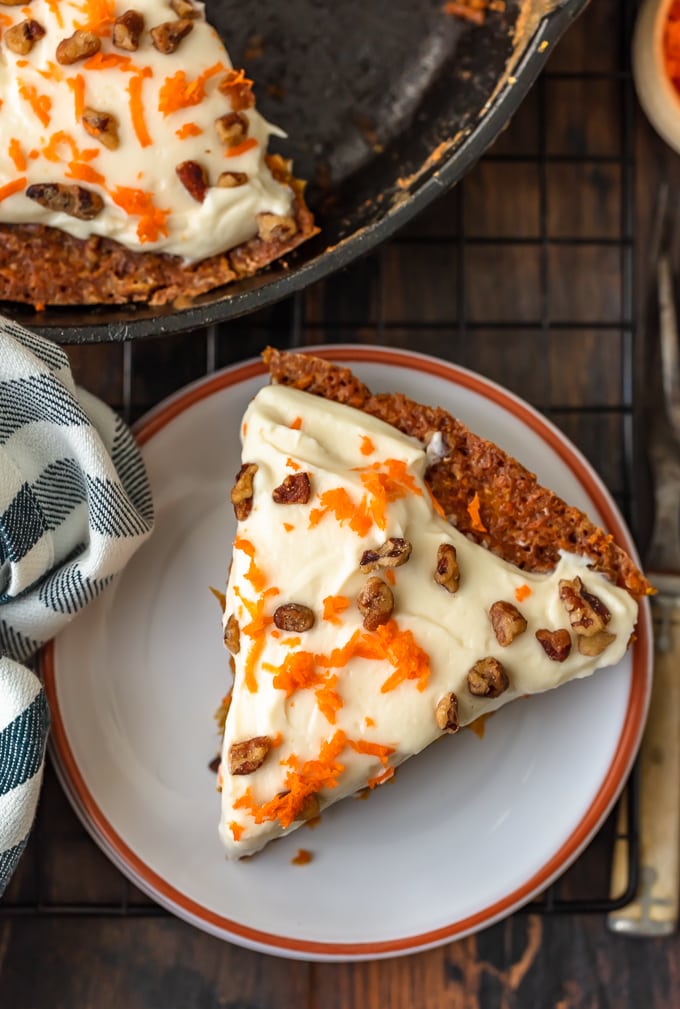 El Skillet Carrot Cake es la manera perfecta de preparar este delicioso postre sin horno. ¡Esta receta fácil de pastel de zanahoria con piña es tan húmeda, tan sabrosa y tan simple! Y lo estamos completando con el mejor glaseado de queso crema para pastel de zanahoria, ¡porque no estaría completo sin él! Una rebanada triangular de pastel de zanahoria en un pequeño plato blanco