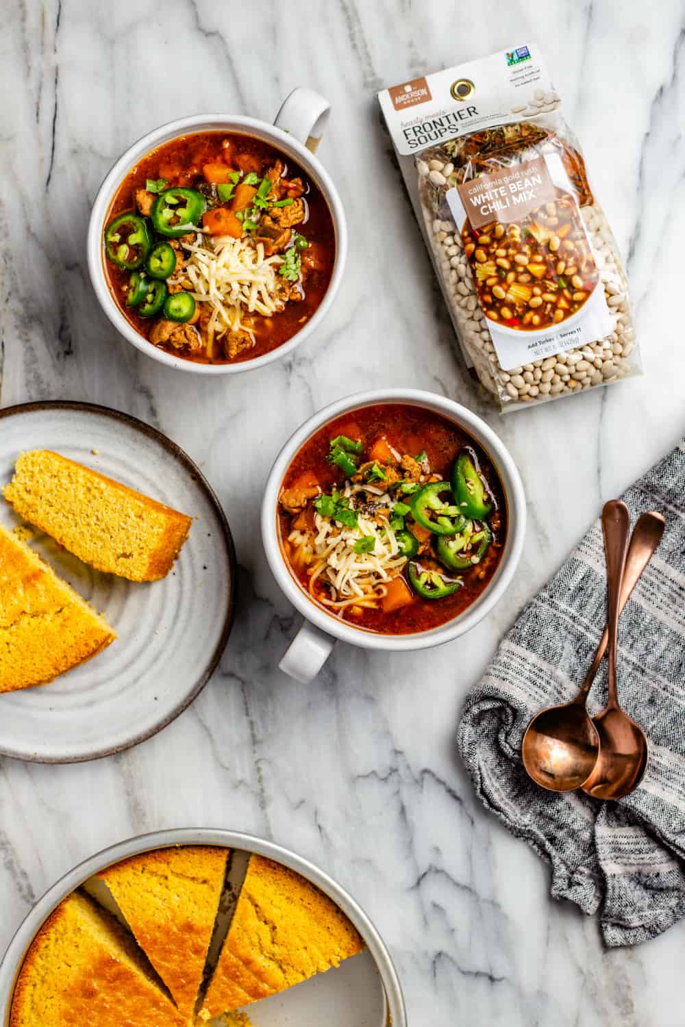 Ciotole di chili di pollo con fagioli bianchi accanto a piatti di pane di mais