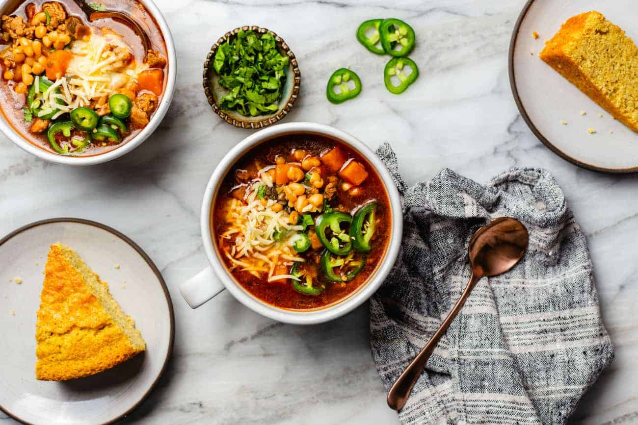 Peperoncino di fagioli bianchi in ciotole su un bancone accanto a pane di mais affettato e jalapeños