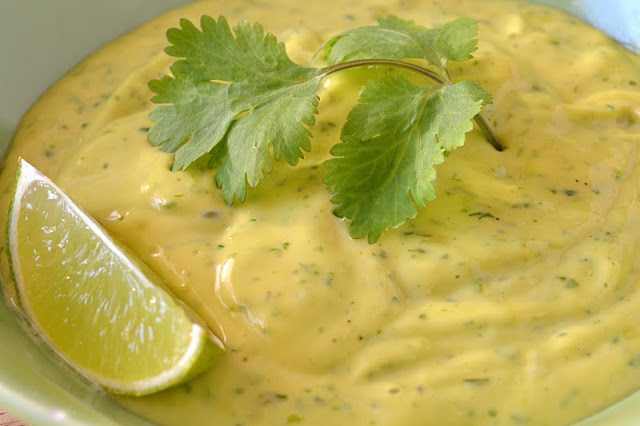 Foto di una ciotola di zucchine avariata con birra e lime e aioli di coriandolo guarniti con una foglia di coriandolo e uno spicchio di lime.
