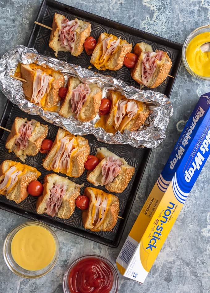 Questi spiedini di panino con burro all'aglio e formaggio sono una svolta per un vecchio classico. Panini al prosciutto, formaggio, tacchino e arrosto di manzo conditi con burro all'aglio e cotti alla perfezione in pacchetti di alluminio; Un pranzo o una cena così divertenti e deliziosi!