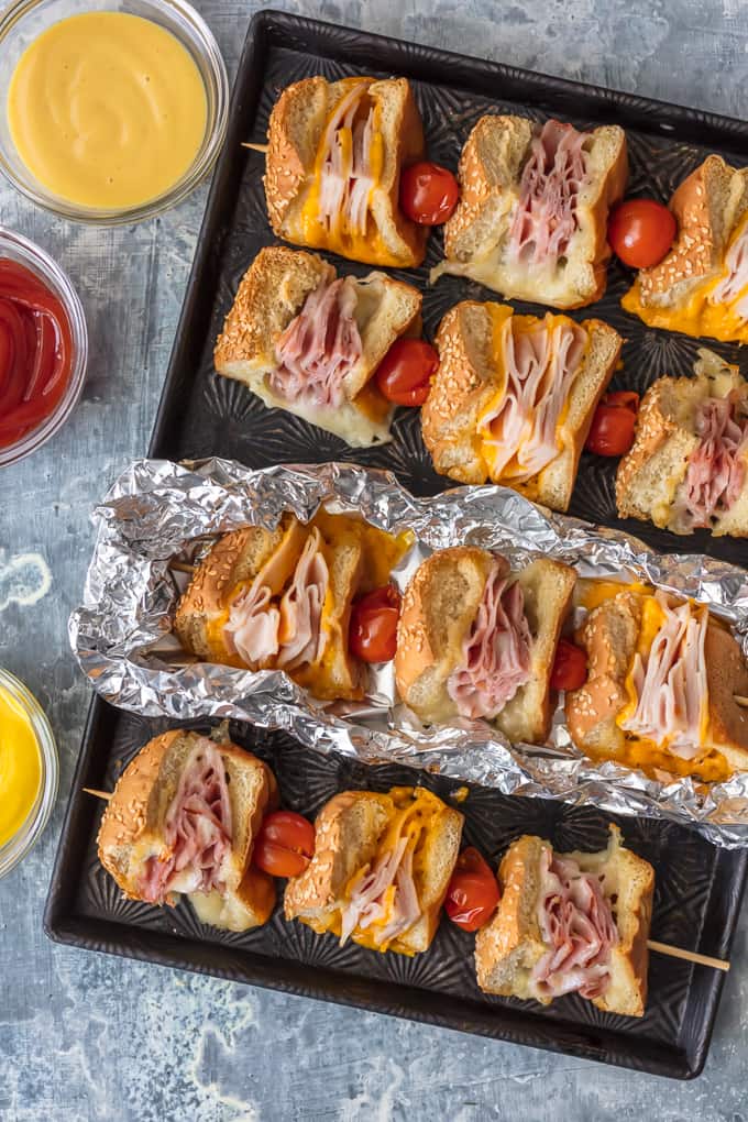Questi spiedini di panino con burro all'aglio e formaggio sono una svolta per un vecchio classico. Panini al prosciutto, formaggio, tacchino e arrosto di manzo conditi con burro all'aglio e cotti alla perfezione in pacchetti di alluminio; Un pranzo o una cena così divertenti e deliziosi!