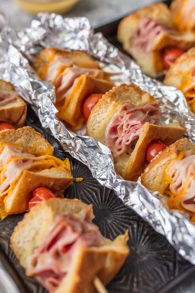 Questi spiedini di panino con burro all'aglio e formaggio sono una svolta per un vecchio classico. Panini al prosciutto, formaggio, tacchino e arrosto di manzo conditi con burro all'aglio e cotti alla perfezione in pacchetti di alluminio; Un pranzo o una cena così divertenti e deliziosi!