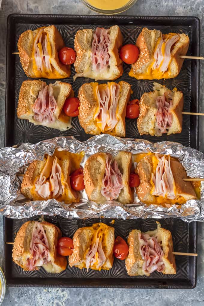 Questi spiedini di panino con burro all'aglio e formaggio sono una svolta per un vecchio classico. Panini al prosciutto, formaggio, tacchino e arrosto di manzo conditi con burro all'aglio e cotti alla perfezione in pacchetti di alluminio; Un pranzo o una cena così divertenti e deliziosi!