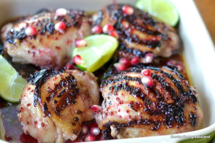 Cosce di pollo glassate al melograno e lime in una teglia verde con semi di melograno e spicchi di lime freschi