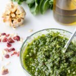 Verticale da vicino del pesto di mirtilli e spinaci ricetta in una ciotola con una bottiglia di olio d'oliva in background