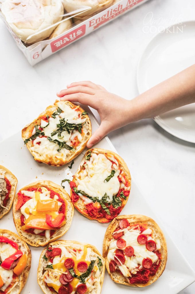 La mano del bambino che raggiunge per una pizza inglese del muffin