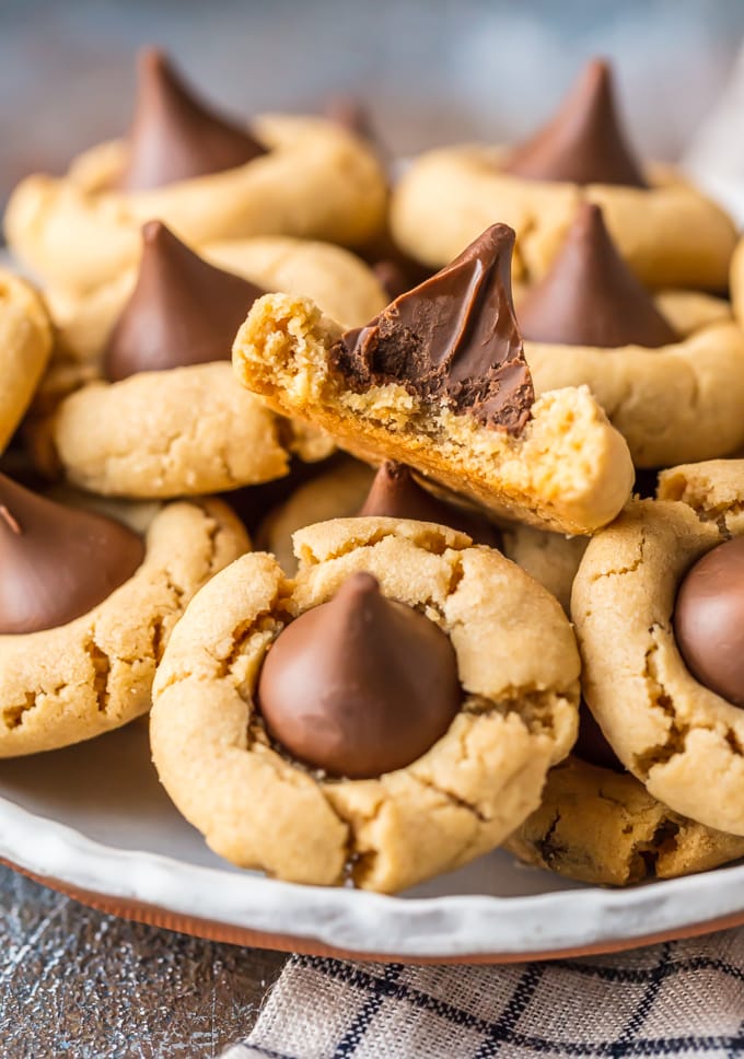 I fiori di burro di arachidi sono una ricetta classica per biscotti facile da preparare e che tutti amano. Questa MIGLIORE ricetta di biscotti al burro di arachidi appartiene alla nostra famiglia da anni. I biscotti con scaglie di cioccolato e burro di arachidi sono perfetti per la cottura a Natale, ma sono anche fatti per essere gustati tutto l'anno, specialmente nei barbecue estivi. Quando si tratta di ricette di biscotti preferite, questi biscotti al burro di arachidi Hershey Kiss non possono essere battuti. 
