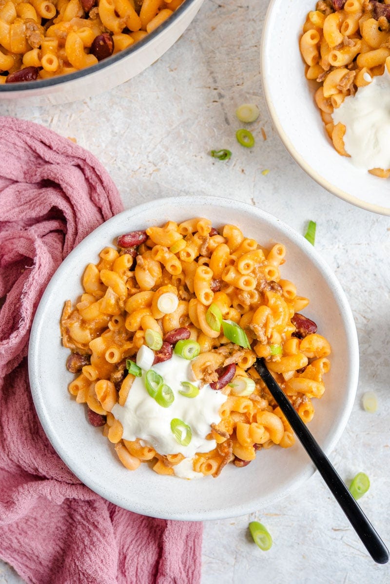 Una foto cenital de chili mac y queso en un tazón cubierto con crema agria y cebolletas