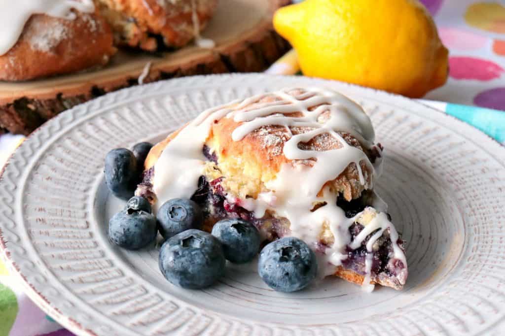 Scone su un piatto con mirtilli freschi, glassa densa e un limone in background