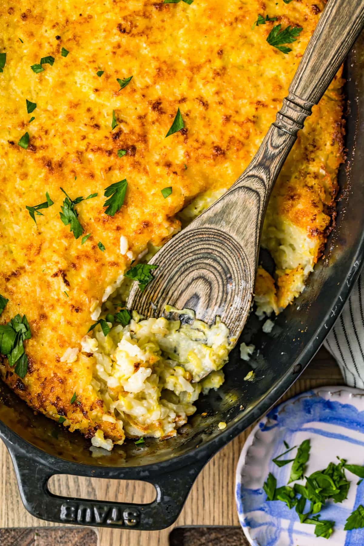 Calabac&iacute;n gratinado al horno en un plato negro con una cuchara de madera