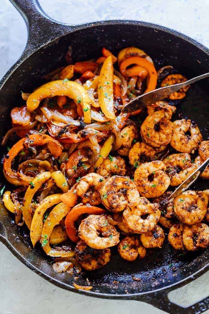 Skillet Shrimp Fajitas, peppers and onions in a cast iron pan with tongs