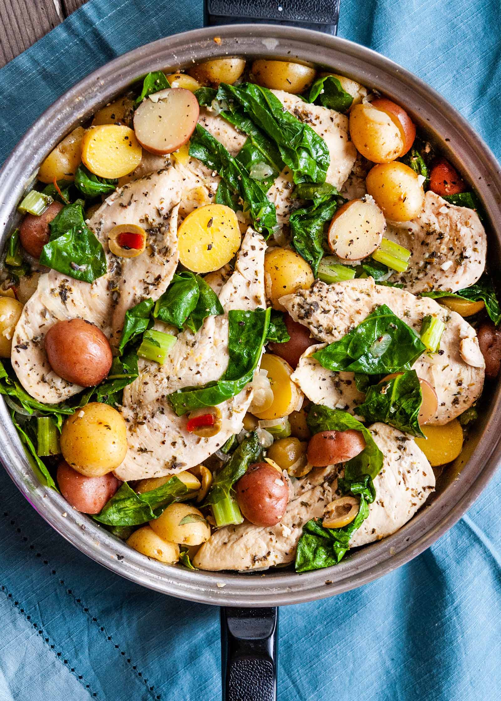 French Chicken Recipe in Skillet-chicken, potatoes, olives and swiss chard in skillet on blue cloth