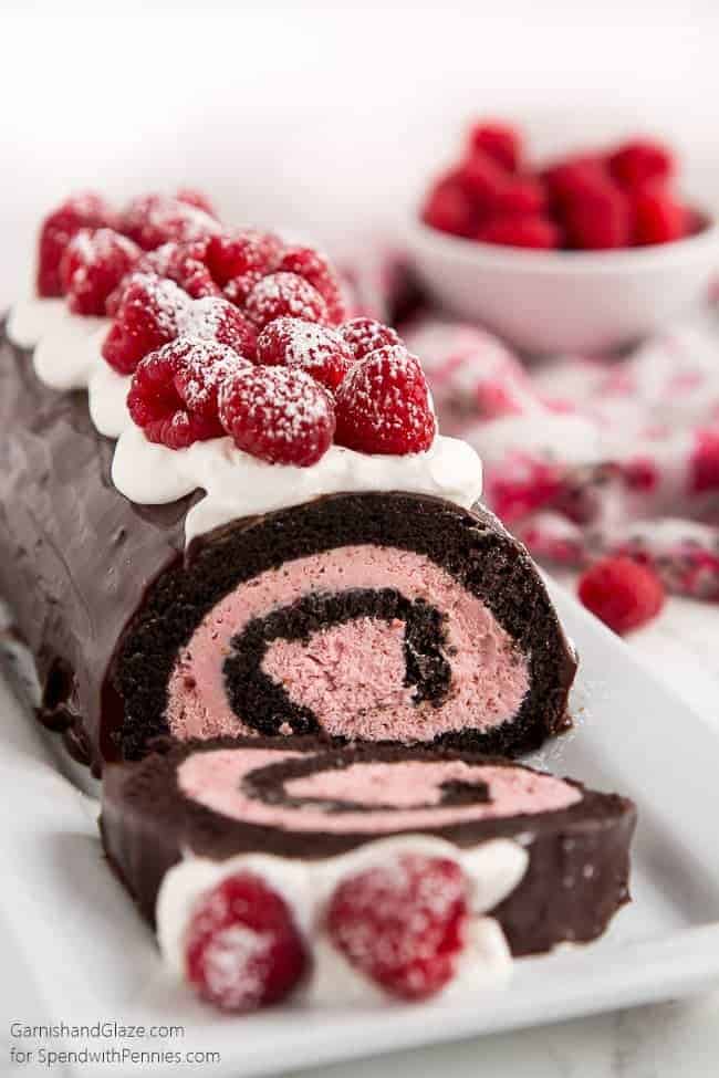 Raspberry Chocolate Swiss Roll topped with berries and a bowl of raspberries in the background