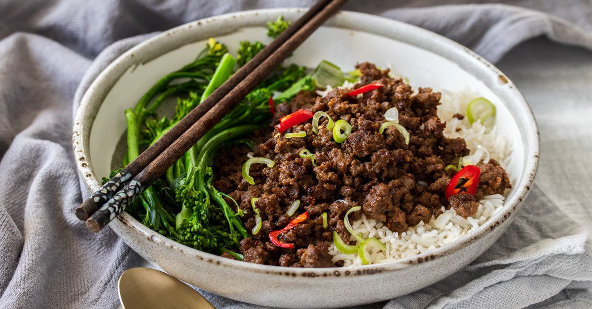 Uma tigela cinza cheia de arroz, pimentão picado e brócolis com pauzinhos por cima