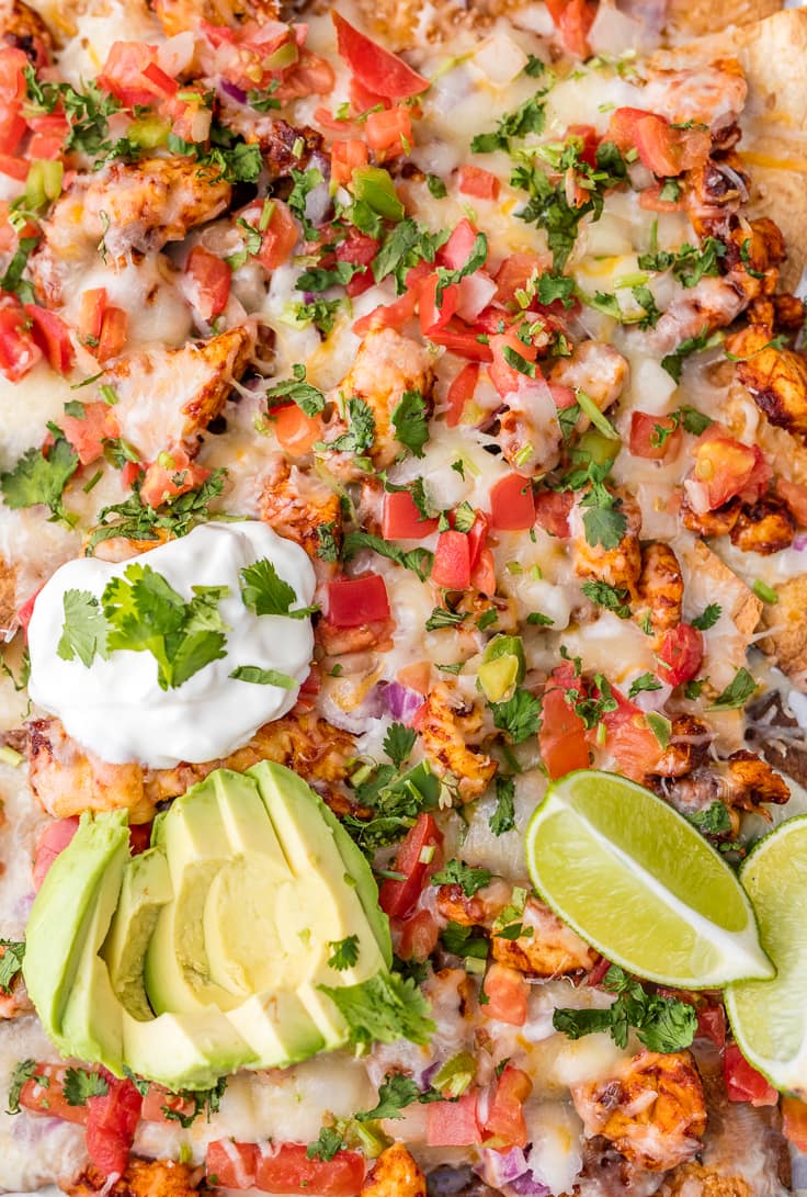 Nachos de frango são ótimos para alimentar uma multidão! Esta receita de nachos de frango assado com limão e tequila é simplesmente INCRÍVEL! Estes nachos frigideiras fáceis são tão deliciosos e perfeitos para qualquer ocasião. close-up em nachos de frango cobertos com pico de gallo, creme de leite e abacate