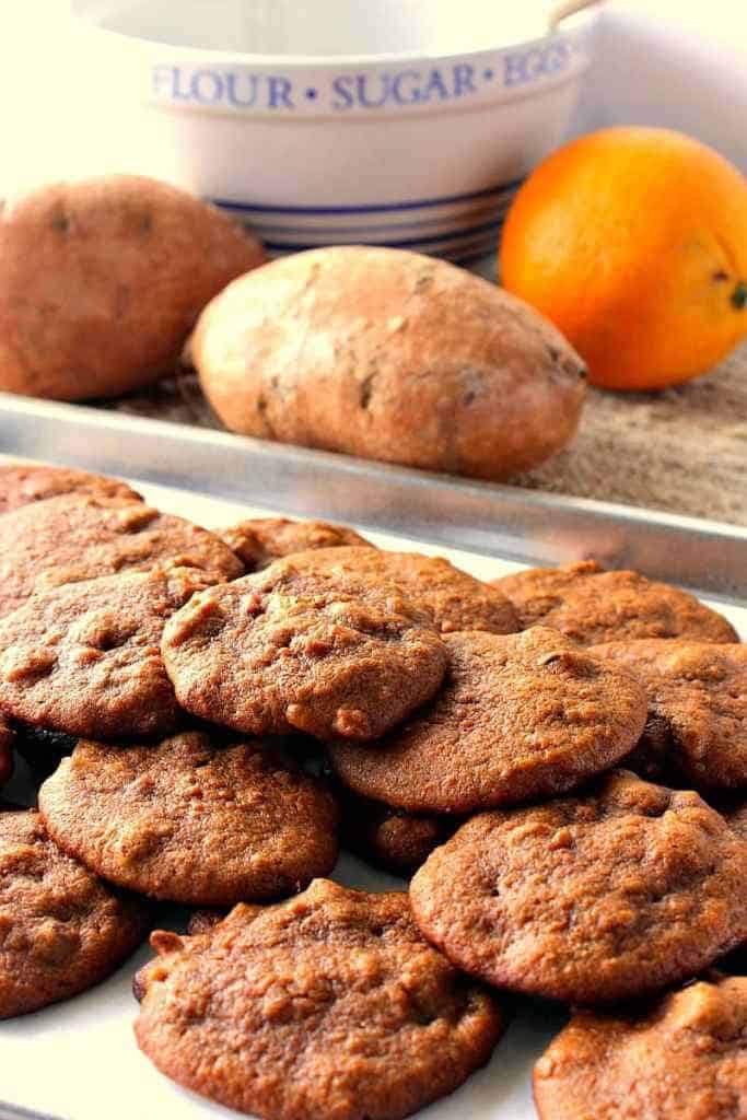 Bandeja de biscoitos da batata doce de Amish no primeiro plano e batatas doces e uma laranja no fundo.