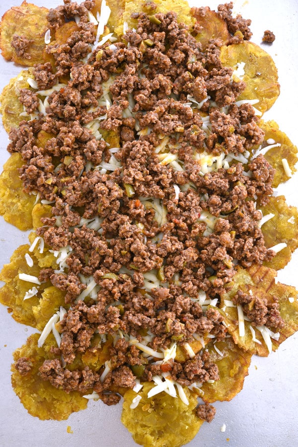 Camadas de tostones, queijo e hash em uma bandeja de biscoitos nacho tostone