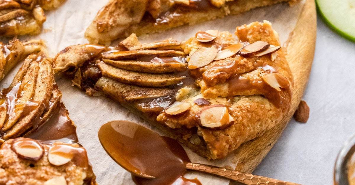 Uma crostata recheada com maçã e regada com molho de caramelo em uma placa de madeira com fatias de maçã no fundo