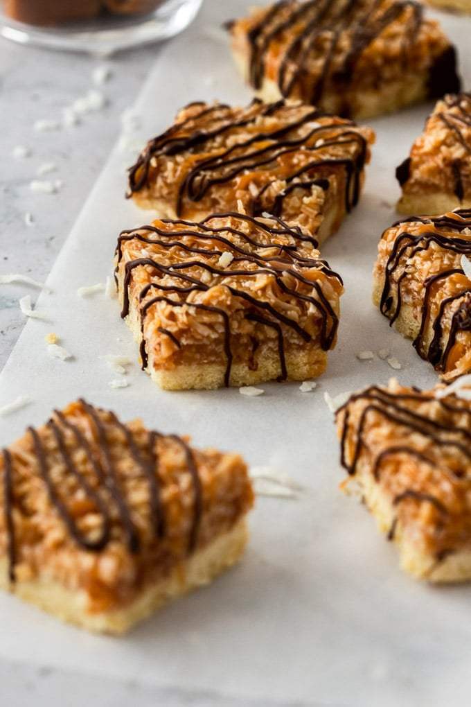 Un grupo de barras de coco con caramelo, rociadas con chocolate en un trozo de papel para hornear