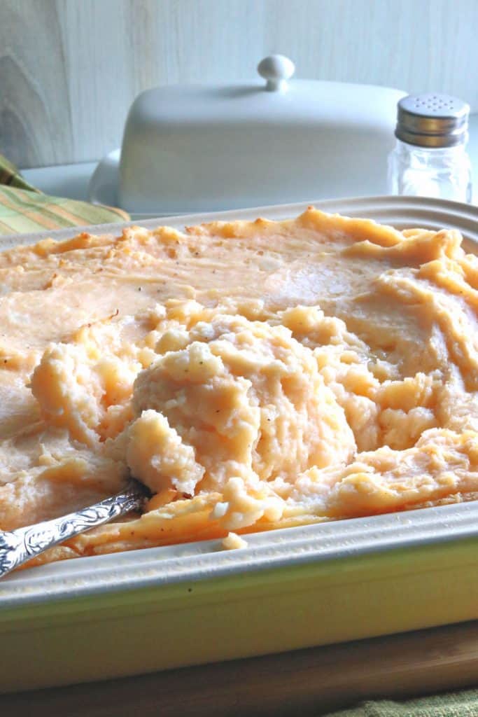 Uma foto vertical do close up de uma caçarola recheada com caçarola de purê de queijo rábano com uma colher de servir.