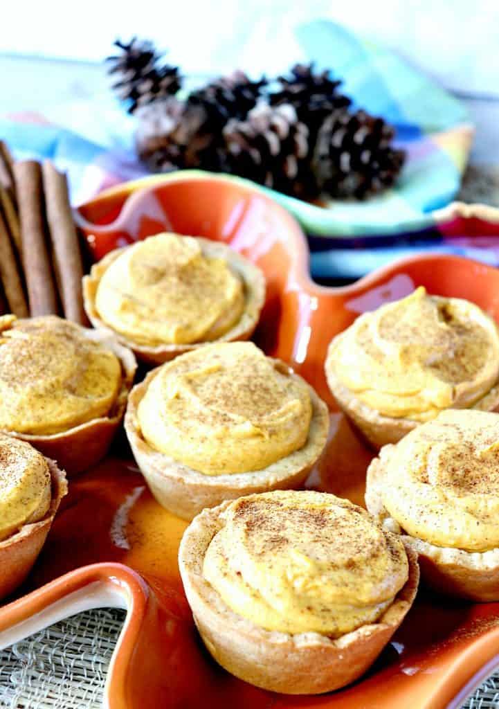 Imagem vertical de tortinhas de bolo de queijo de abóbora em uma placa de folha de laranja para a visão geral de receitas de sobremesas de ação de Graças.