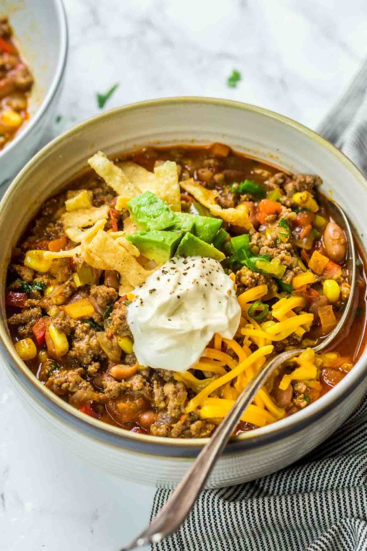 Sopa de taco em uma tigela com uma sopa coberta com creme de leite, abacate, tortilha e pimentão.