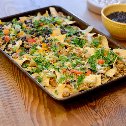 Nachos, mexicano, queijo, peru moído, feijão preto, pimentão e coentro.