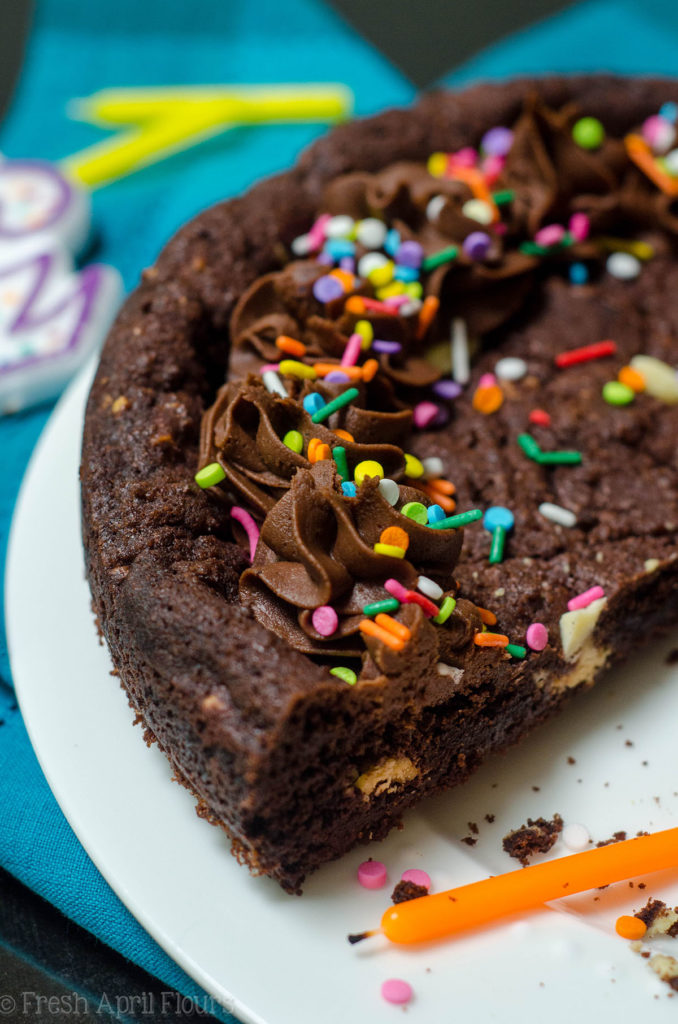 Bolo Triplo de Biscoito de Chocolate: Bolo de biscoito de chocolate escuro cheio de pedaços de chocolate branco-amarelado e coberto com uma cobertura de chocolate.