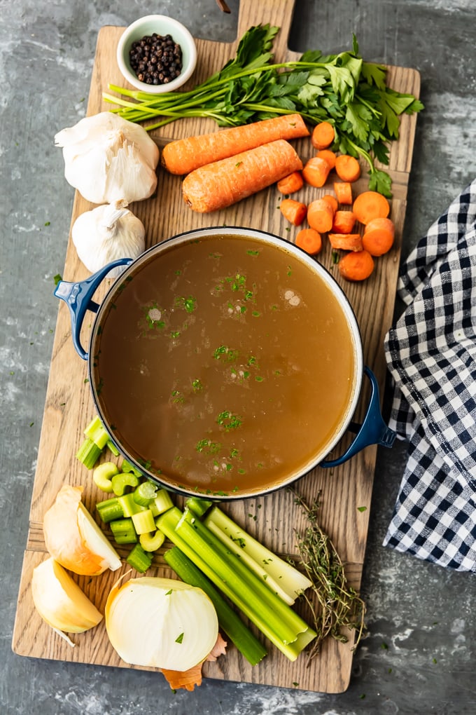 Cómo hacer caldo de pollo: las zanahorias, el apio y el ajo se sientan en una tabla de cortar, junto a una olla de caldo de pollo