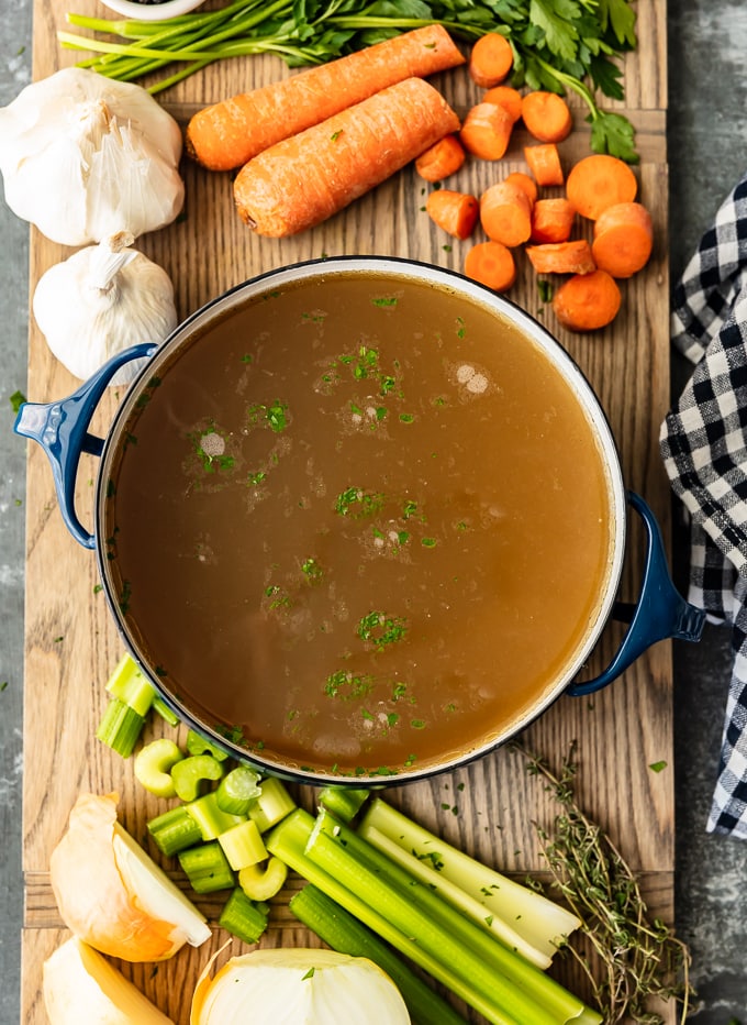 Una olla de caldo de pollo casero rodeado de zanahorias, ajo y apio