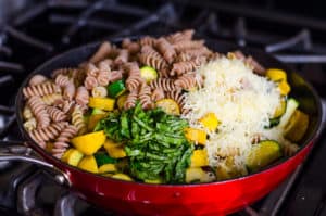 Macarrão, legumes, manjericão e queijo em uma panela no fogão