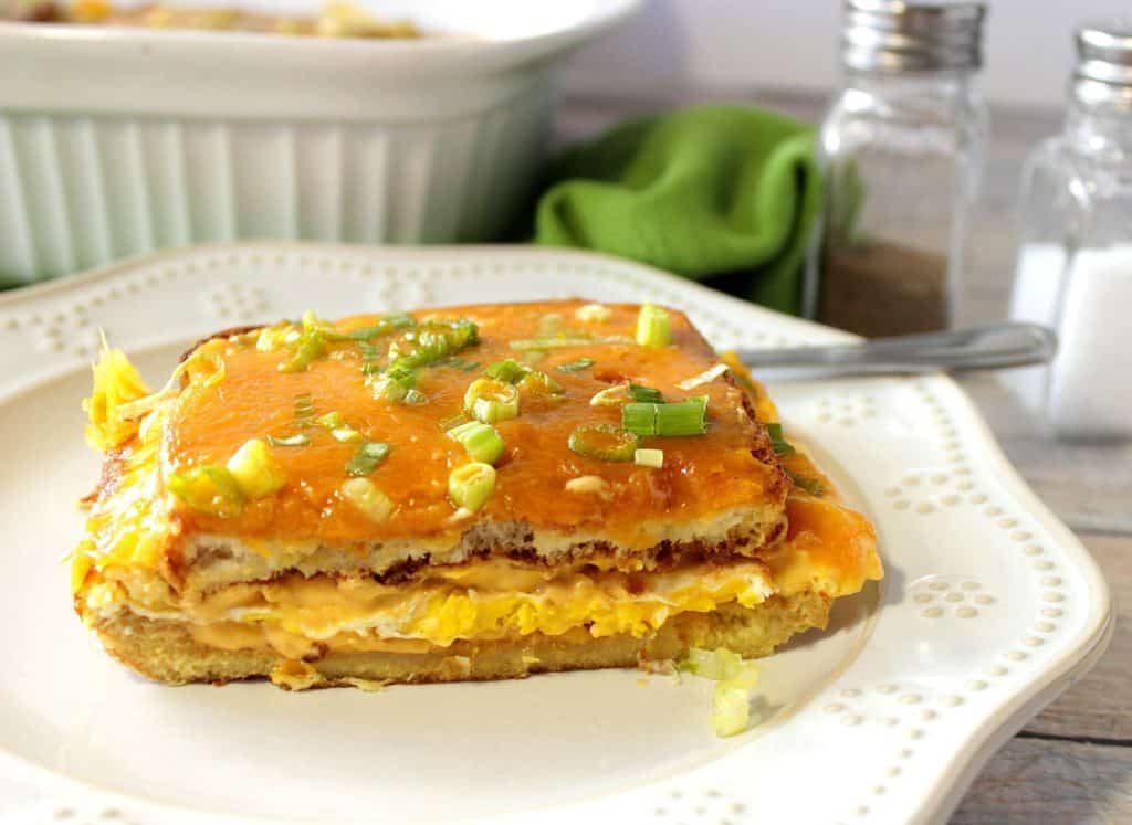 Uma fatia de caçarola de sanduíche de ovo em um prato branco com cebolinha e queijo cheddar.