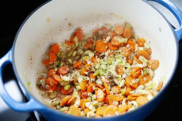 Cenouras, cebolas e aipo no fundo de um forno holandês para fazer sopa de macarrão cremosa e saudável.