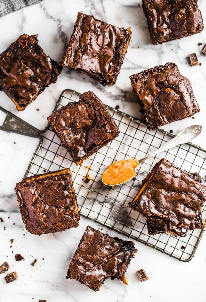 Brownies de abóbora são uma receita fácil de sobremesa de outono, perfeita para o Halloween ou o Dia de Ação de Graças. Adicione uma camada de abóbora aos seus brownies para algo divertido e delicioso! Brownies de abóbora perfeitos, dispostos em torno de uma gradinha para esfriar, com uma colher de sopa de abóbora
