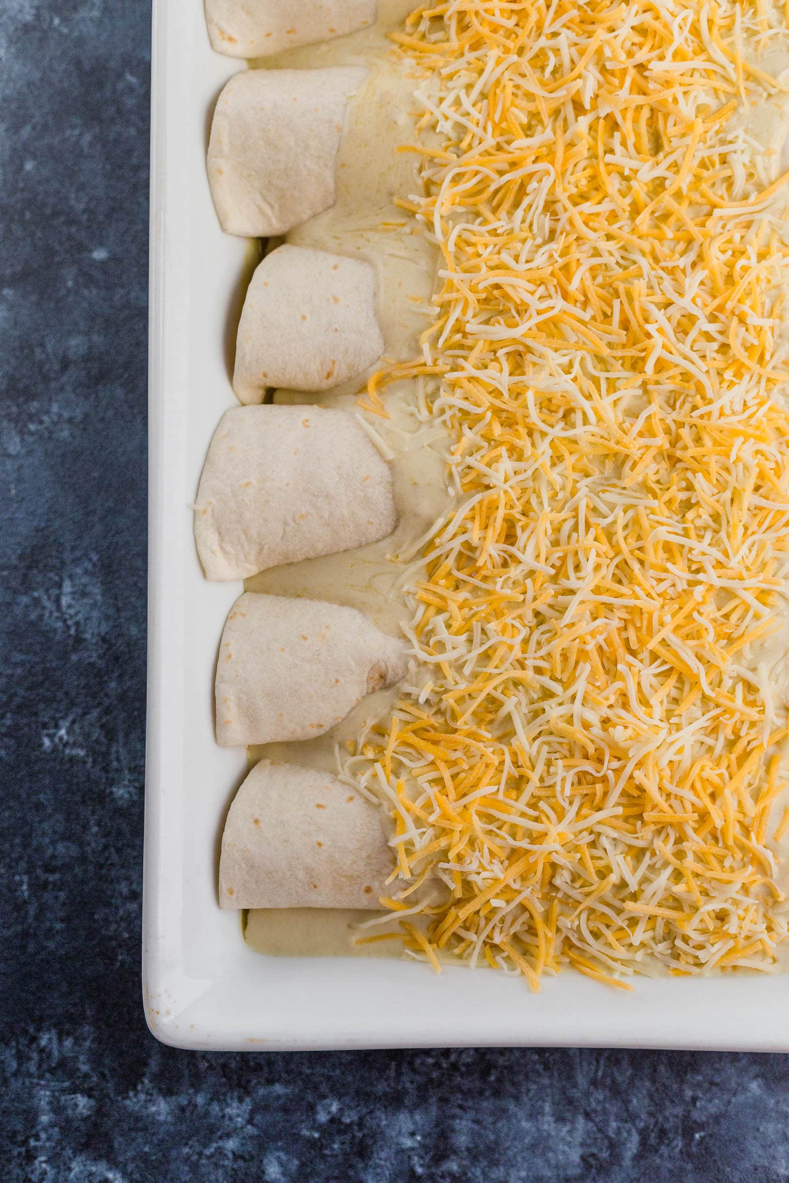Un plato de enchiladas cubiertas con queso rallado, antes de hornear