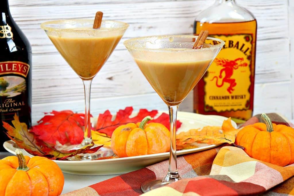 Dois martinis da especiaria da abóbora com um fundo de madeira branco e um guardanapo deixado cair e mini abóboras.