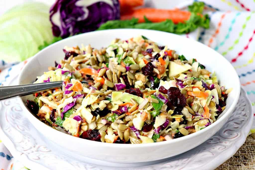 Salada de repolho colorida em uma bacia branca com uma colher e um guardanapo colorido no fundo.