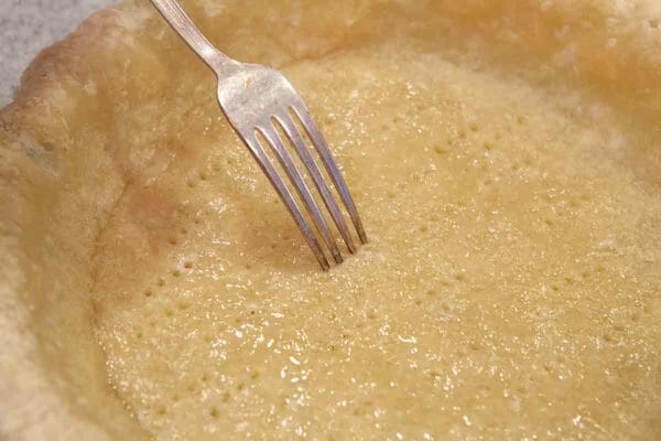 picar o fundo da massa de torta semi-assada com os dentes de um garfo