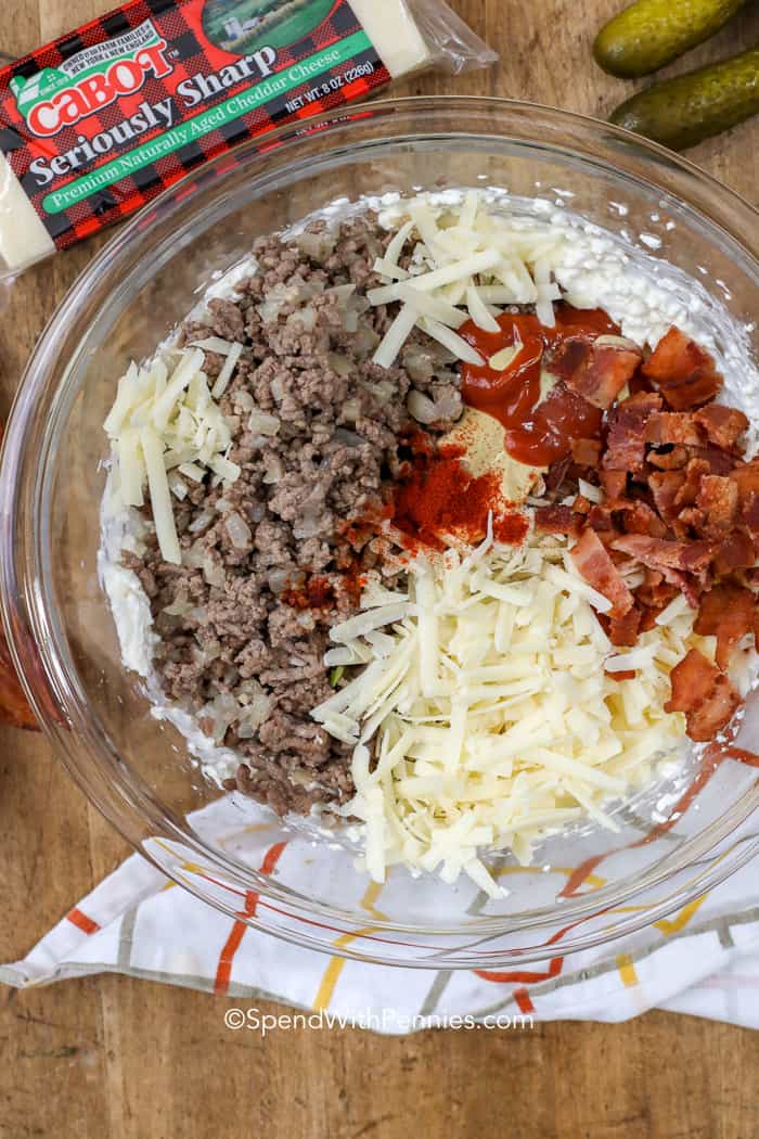 Un tazón lleno de ingredientes para hamburguesas como carne molida, salsa de tomate, tocino y queso.