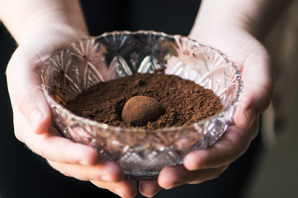 Manos sosteniendo un recipiente de vidrio con cacao en polvo y una trufa de chocolate