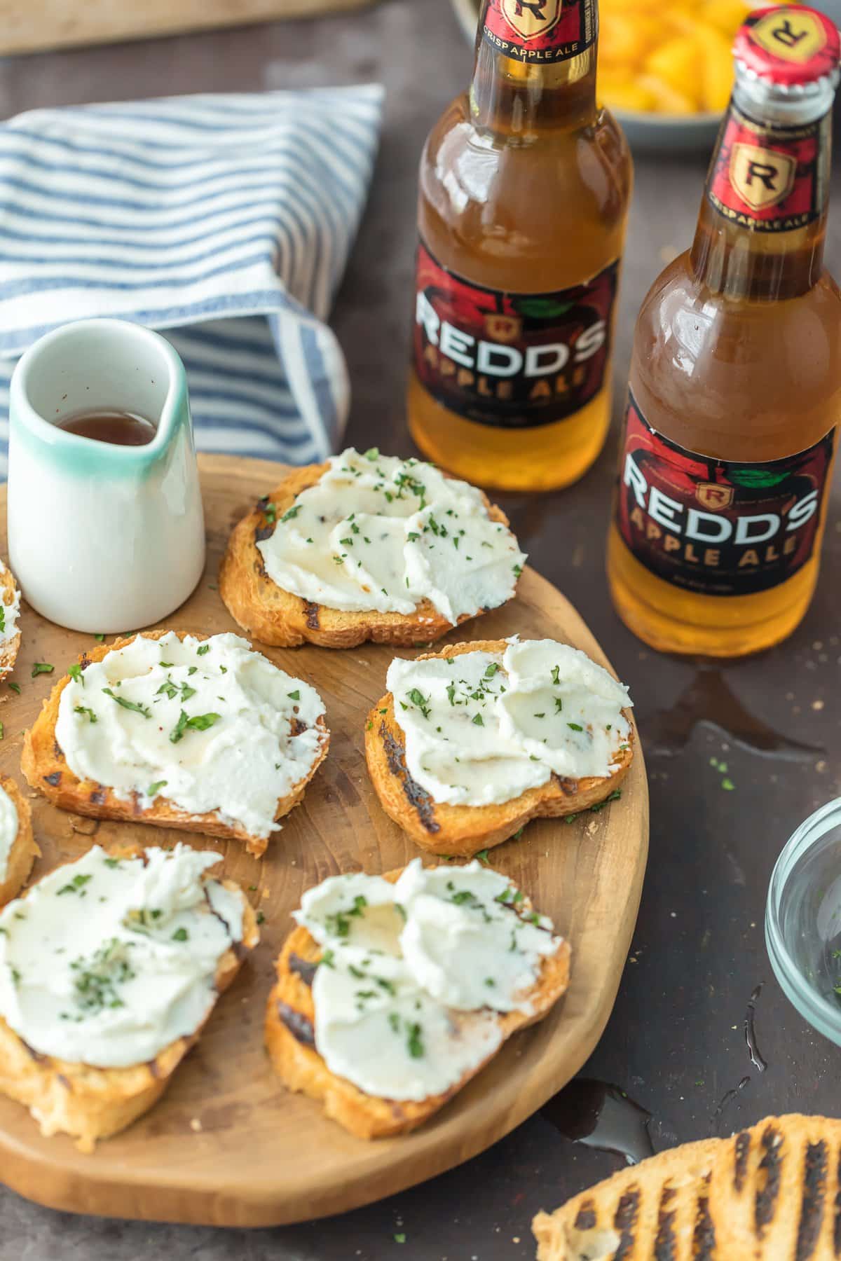 Crostini de queijo de cabra em uma bandeja ao lado de duas garrafas de cerveja