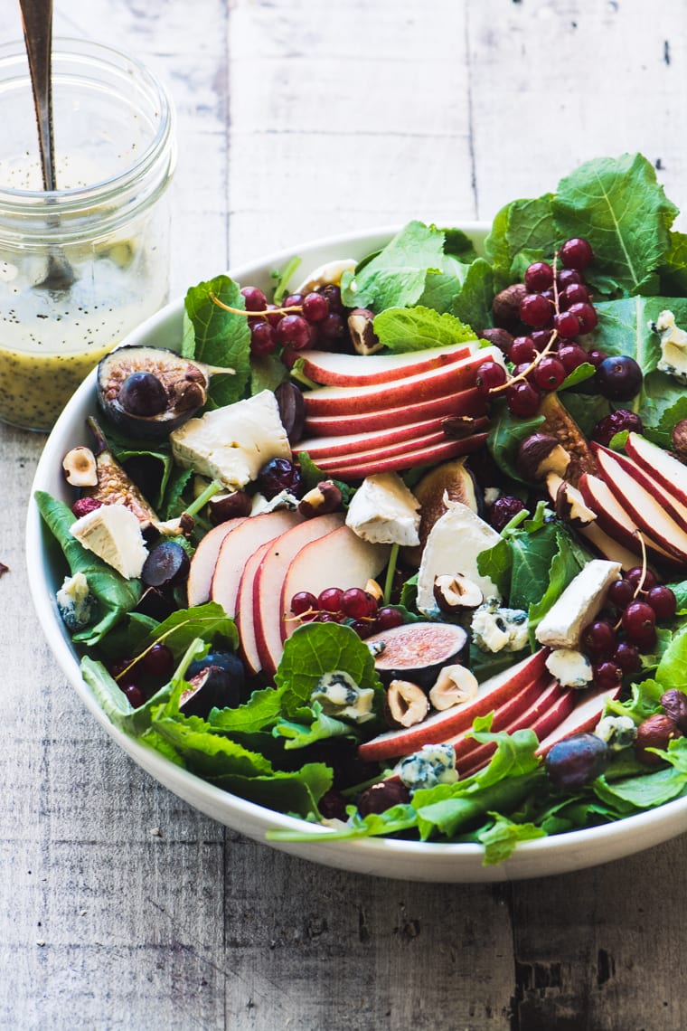 Ensalada de col rizada y fruta de otoño con aderezo de sidra de semillas de amapola ~ esta es la reina de las ensaladas de otoño, con pera, arándanos, higos, granada y uvas, todo mezclado con una cremosa vinagreta de sidra. #fall #healthy #paleo #glutenfree # whole30 #vegetarian #fallsalad #fruitsalad #fallfruit #poppyseeddressing #bestpoppyseeddressing #holidaysalad #thanksgivingside #superfood #kale Ensalada de frutas de col rizada y otoño con aderezo de sidra de semillas de amapola en una mesa de madera