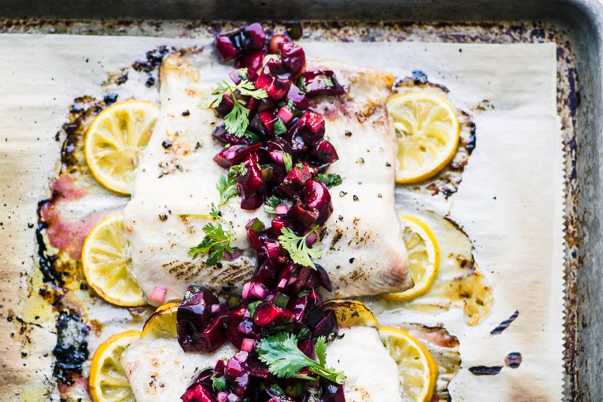 Peixe branco grelhado com molho de cereja e limões em uma assadeira