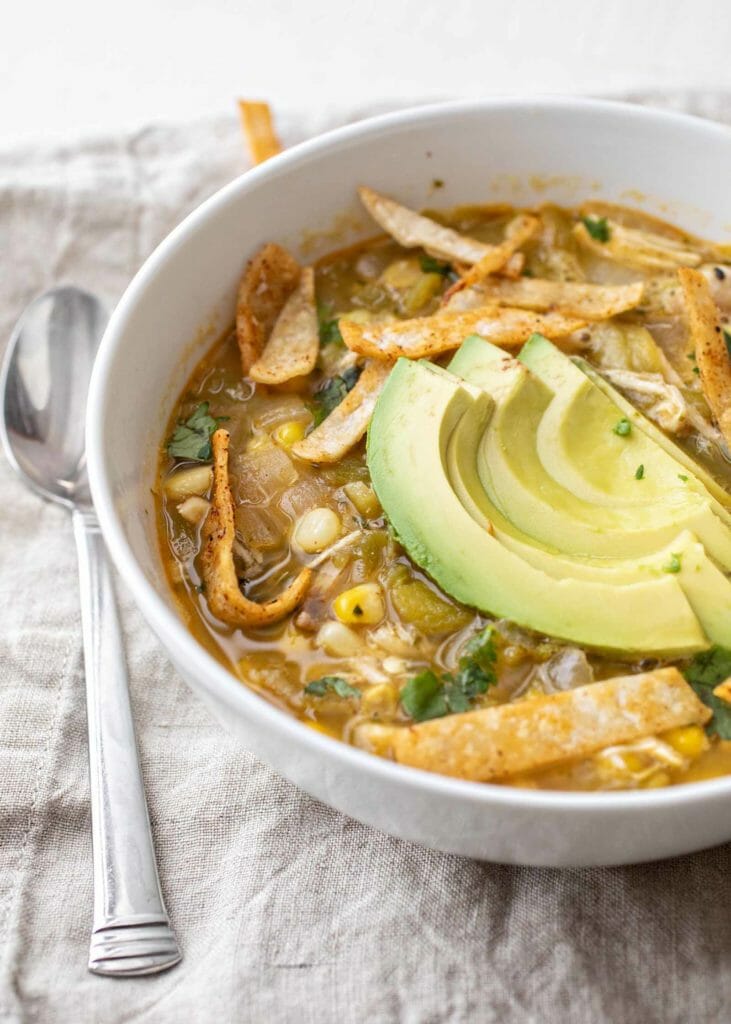 Uma tigela de sopa de pimenta verde com batatas fritas de abacate e tortilla